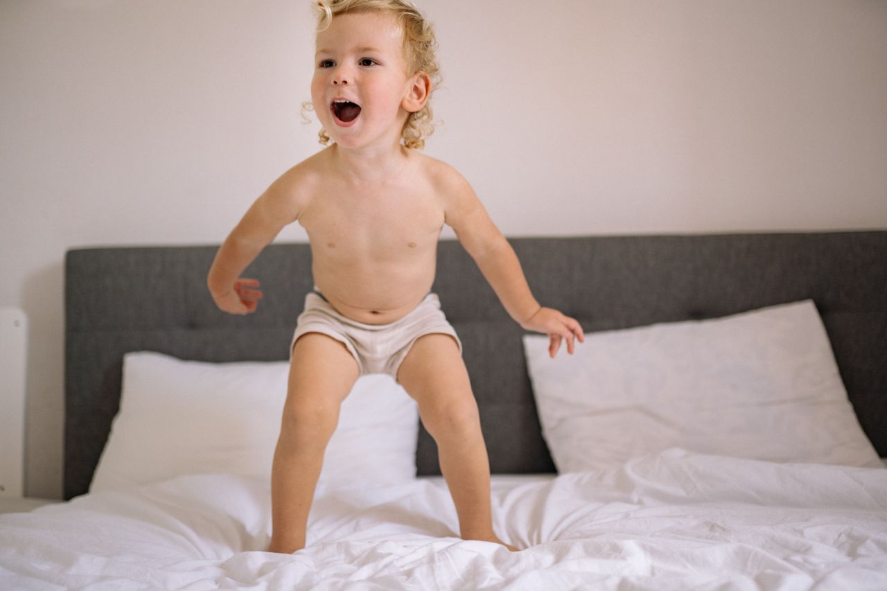 Adorable child jumping energetically on a bed in a cozy bedroom environment.